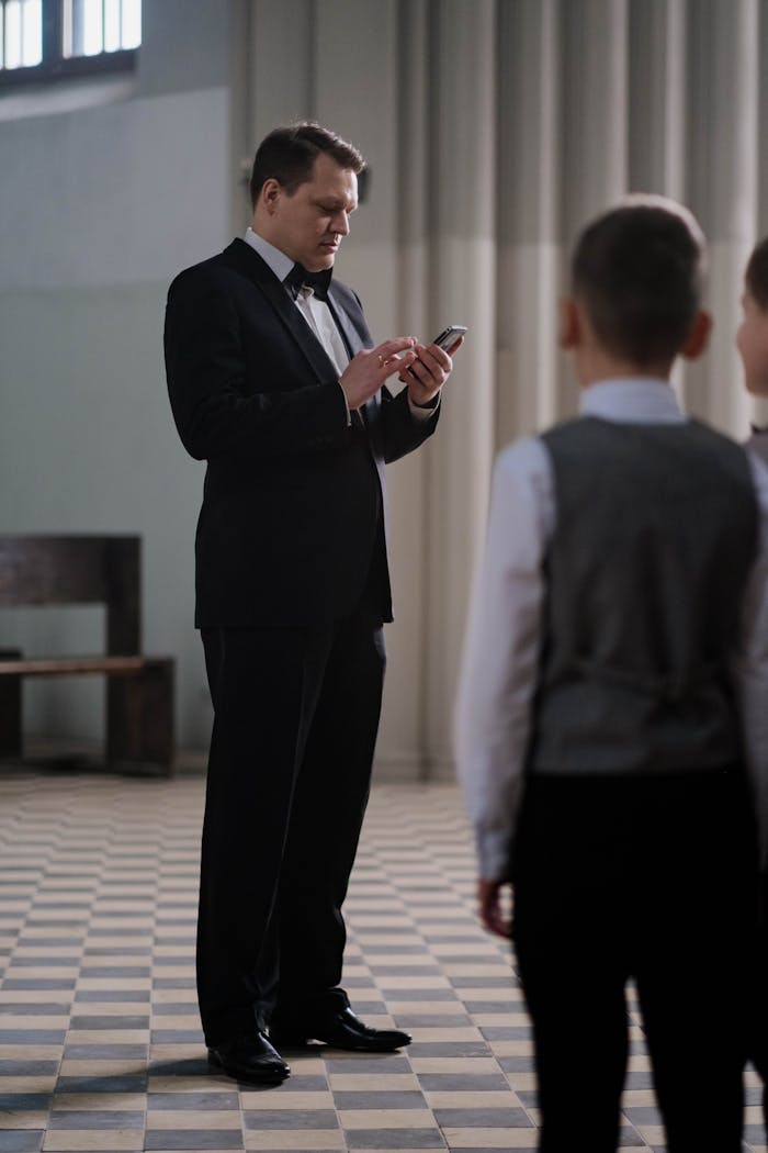 Conductor in tuxedo checks smartphone in choir practice with children.